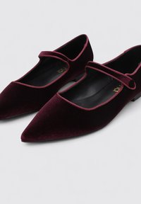 Bailarinas de terciopelo burdeos con punta afilada y una sola tira cruzando el pie. Tacón bajo en bloque, forro interior suave y detalle de costura sutil.