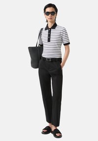 Polo tričko s černobílými pruhy a černým límečkem, černé kalhoty, černý opasek, černá kabelka a černé pantofle. Hladké textury po celém outfitu.