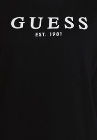 Maglietta nera in cotone con grande scritta bianca "GUESS" e "EST. 1981" stampata sotto. Tessuto liscio, design classico con scollo rotondo.