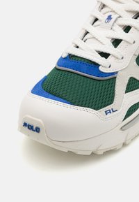 Vit sneaker med grön meshovandel, blå detaljer och gråa överlägg. Har märkt hälflik och texturerad sula. Snörningsdesign.