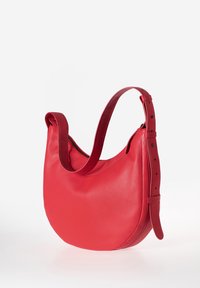 Rode leren handtas met een gladde textuur, ronde vorm en een enkele verstelbare schouderriem. Voorzien van een ritsluiting en subtiele hardware-accenten.