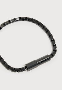 Μαύρο μεταλλικό βραχιόλι με ορθογώνιες συνδέσεις και χαραγμένη κυλινδρική αγκράφα σε ανοιχτό φόντο.