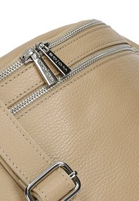 Beige kožená taška přes rameno s dvojitým zipem ve stříbrné barvě, hladkým povrchem a metalickým sponou na popruhu.