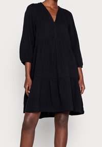 Svart lager-på-lager klänning gjord av lättviktig tyg. Har en V-ringning, ballongsärmar och en avslappnad passform. Subtil textur tillför djup.