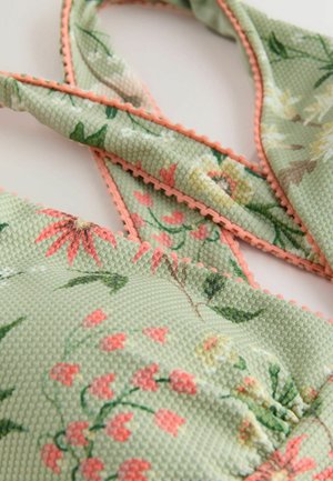 Floral-patterned green fabric with textured surface. Features coral trim along edges, with a crisscross strap design.