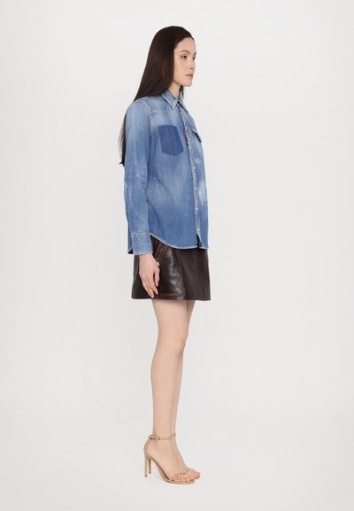 Denim button-up shirt in blue with a chest pocket paired with a brown leather mini skirt and nude high-heeled sandals.