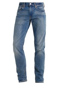 Siniset farkut, joissa on klassinen suora lahje, viiden taskun muotoilu, vetoketjullinen haarakiinnitys ja metalliset koristetapit.