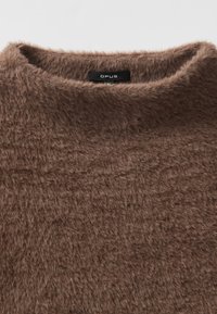 Brauner, flauschiger Pullover mit hohem Kragen, hergestellt aus einem weichen Material. Das Etikett "OPUS" ist am Kragen sichtbar.