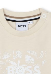 Beige katoenen t-shirt met korte mouwen en een ronde hals, met een witte bloemenprint en het "BOSS" logo op de voorkant.