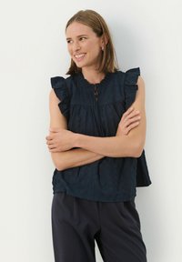 Marineblaue, strukturierte Bluse mit gerafften Ärmeln und einem knöpfbaren Schlüsselloch-Ausschnitt. Kombiniert mit dunklen Hosen, die ein lässiges Design präsentieren.