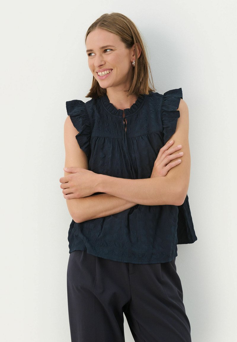 Marineblaue, strukturierte Bluse mit gerafften Ärmeln und einem knöpfbaren Schlüsselloch-Ausschnitt. Kombiniert mit dunklen Hosen, die ein lässiges Design präsentieren.