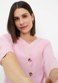 Light pink cardigan, lightweight knit, v-neck design, short sleeves, three buttons at the front, smooth texture, casual style.