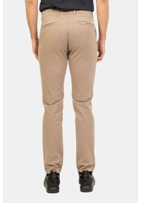 Pantaloni beige a taglio slim, con una texture liscia, due tasche posteriori e fissati con una cintura, abbinati a scarpe nere.
