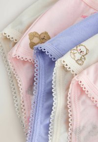 Des vêtements pour bébé en tissu pastel doux avec des bords en dentelle festonnée et des motifs brodés d'ours en peluche en marron et blanc, pliés étroitement ensemble.