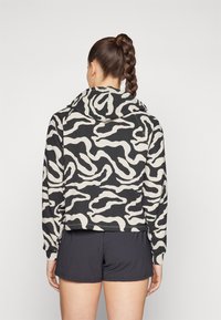 Sort og beige hættetrøje med et bølget mønster, der har en frontlomme og hætte, parret med sorte shorts.