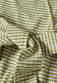 Zielono-biała tkanina w paski o teksturowanym, pomarszczonym wyglądzie, z naprzemiennymi poziomymi liniami o różnych szerokościach.