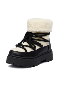 Zimowy but na platformie z grubą czarną podeszwą, kremowym futrem z owczej wełny na górze i czarnymi krzyżującymi się sznurowadłami owiniętymi wokół kostki.