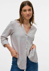 Chemise légère grise, à boutons, avec un design sans col, manches longues retroussées aux coudes, et coupe décontractée. Fabriquée en tissu doux.