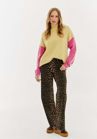 Prevelký žltý pletený sveter s ružovými rukávmi, spárovaný s nohavicami so zvieracím vzorom a hnedými platformovými topánkami. Hladké textúry po celom povrchu.