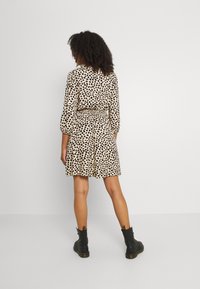 Beige dress with black leopard print, fitted waist, long sleeves, and flared skirt. Paired with black ankle boots and textured fabric.