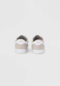 Μπεζ δερμάτινα αθλητικά παπούτσια με λευκή φτέρνα, με υφή επιφάνειας και διακριτική λεπτομέρεια λογότυπου στο πίσω μέρος. Λευκή σόλα από καουτσούκ.