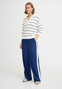 Strikket sweater i creme med marineblå striber og hulmønsterdetaljer, parret med brede marineblå bukser med hvide sidelister. Struktureret stof.