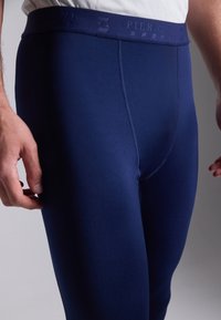Marineblauwe sportlegging met een brede tailleband en een reliëflogo. Glad, rekbaar materiaal, aansluitend ontwerp, geen zichtbare patronen.