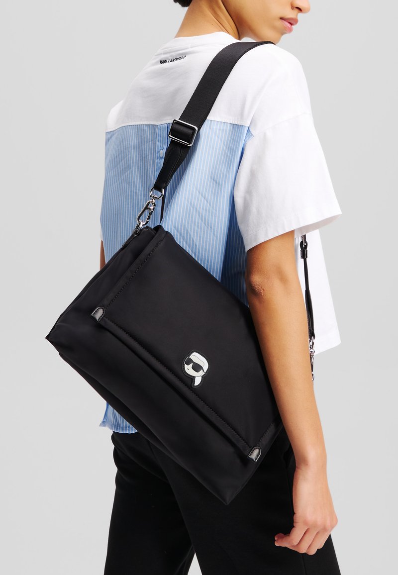 Borsa a tracolla nera realizzata in materiale testurizzato, con un logo distintivo, una tracolla regolabile e un design elegante con un compartimento con zip.