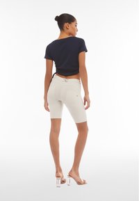 Top corto de color azul marino con mangas cortas, combinado con pantalones cortos de ciclista beige con una cintura alta y costuras de acento, llevados con sandalias de tacón transparente.