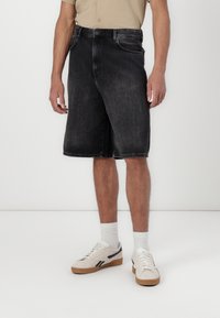 Mørke denimshorts med en afslappet pasform, fem-lomme design og frynset kant. Båret med hvide sokker og cremefarvede sneakers.