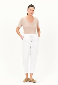 T-shirt beige a scollo a V con maniche corte, abbinato a pantaloni in lino bianchi con coulisse e due tasche frontali, indossati con mocassini marrone chiaro.