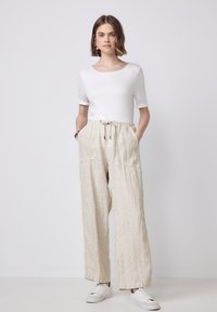 Witte T-shirt met korte mouwen, gecombineerd met lichtbeige, verticaal gestreepte, loszittende broeken met een elastische tailleband en zijzakken. Witte sneakers.