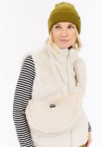 Crème nepbontvest met hoge kraag en rits, gecombineerd met een zwart-wit gestreept langslavenshirt. Olijfgroen gebreid beanie.