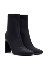 Botas negras hasta el tobillo hechas de tela suave, con punta afilada y un tacón grueso. Las costuras resaltan el diseño elegante.