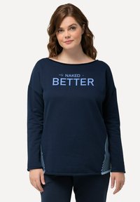 Maglietta a maniche lunghe blu navy con scollatura ampia, caratterizzata dalla scritta "NAKED is BETTER" in testo azzurro e dettagli a righe sui lati.