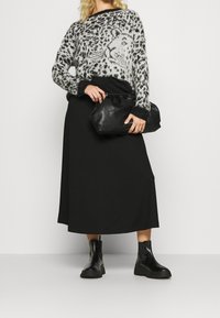 Frau trägt einen grauen und schwarzen Leopardenmuster-Pullover, einen schwarzen Midikleid, schwarze Leder-Stiefeletten und hält eine schwarze Leder-Clutch.