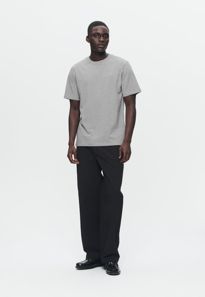 Γκρι κοντομάνικη μπλούζα από βαμβάκι, με στρογγυλή λαιμόκοψη. Συνδυάζεται με άνετο μαύρο παντελόνι και μαύρα παπούτσια, πάνω σε λευκό φόντο.