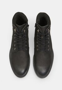 Zapatos de cuero negros con acabado texturizado, punta redonda, diseño de cordones y cremalleras laterales para un acceso fácil. Forro interior suave visible.