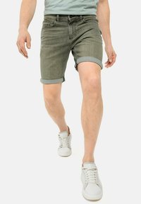 Grijze denim shorts met opgerolde mouwen, voorzakken en riemlussen, gecombineerd met witte sneakers op een effen achtergrond.