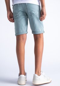 Shorts in denim azzurro chiaro con orli arrotolati, dotati di tasche posteriori e una vestibilità rilassata. Indossati con sneakers bianche su gambe scoperte.