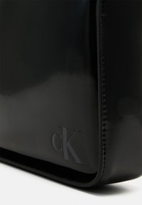 Borsa in pelle verniciata nera con design minimalista, caratterizzata da logo 'cK' in rilievo, texture liscia e linee pulite.