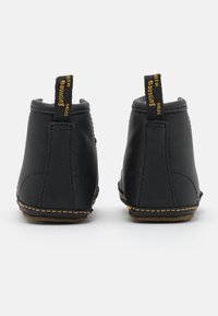 Botas de tornozelo em pele preta com forma arredondada, costura amarela e puxadores na parte de tr�ás rotulados "COM SOLAS ELÁSTICAS".
