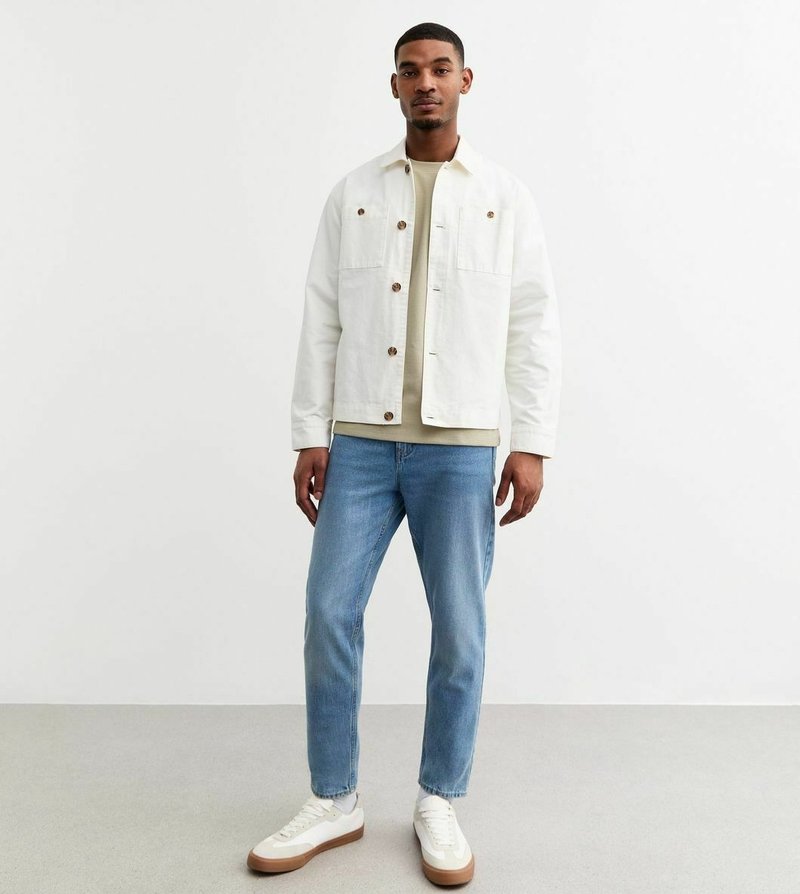 Witte denimjasje met bruine knopen, beige t-shirt, lichtblauwe jeans en witte sneakers met bruine zolen. Eenvoudige, casual kledingoutfit.