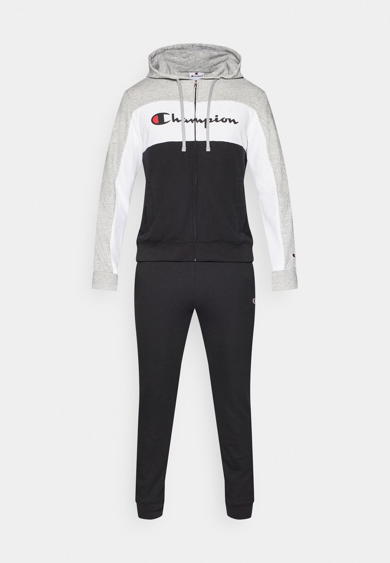 Tuta nero e grigio con felpa con zip e pantaloni stretti. Presenta un pannello centrale bianco e il logo "Champion" in rosso sul petto.