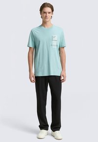 Lichtblauw katoenen T-shirt met een ronde hals, korte mouwen en een tekstprint aan de voorkant. Gecombineerd met zwarte broek en witte sneakers.