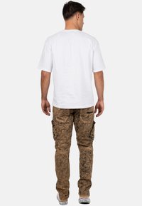 T-shirt bianca in cotone a maniche corte, abbinata a pantaloni cargo marroni con motivo, dotati di tasche laterali e sneakers bianche.