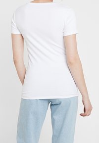 Vit kortärmad t-shirt med rund halsringning, figurnära design och släta textur, tillsammans med ljusblå denimbyxor.