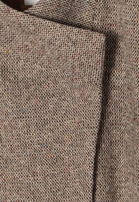 Tejido texturizado en un cálido tono marrón, con motas multicolores en toda su superficie. Material suave y tejido de grosor medio.