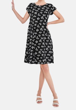 Robe noire à manches courtes avec un motif floral blanc, jupe évasée et coupe décontractée, assortie de sandales blanches à lanières.