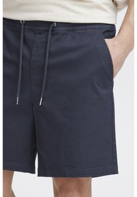 Marineblauwe korte broek gemaakt van een katoenmengsel, voorzien van een elastische tailleband met een trekkoord en zijzakken. Soepele textuur, tot op de knie.